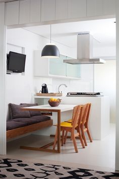 a kitchen table with two chairs and a television mounted on the wall above it, next to a couch