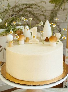 a white cake with mushrooms and daisies sitting on top of a wooden table next to flowers