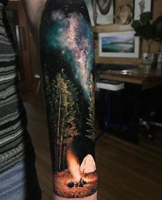 a person with a tattoo on their arm that has a forest scene and stars in the sky