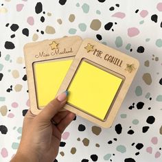 a hand holding a yellow post - it note pad next to a wooden magnet with gold stars