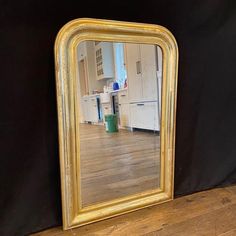 a gold framed mirror sitting on top of a wooden floor next to a black wall