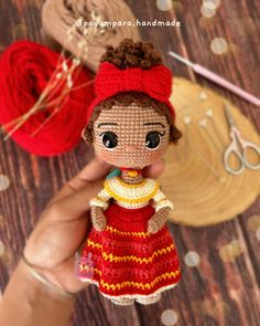 a hand holding a small doll next to some yarn and scissors on a wooden table