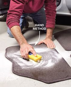 a man is using a sponge to clean the car's floor mat with a yellow brush