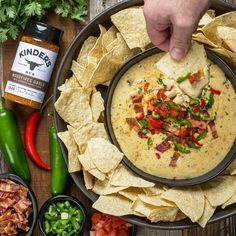 a person dipping tortilla sauce into a bowl with chips and vegetables around it