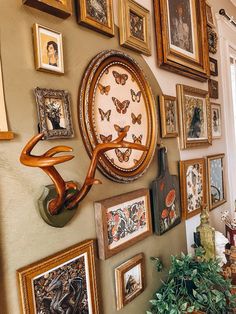 a wall full of framed pictures and paintings with a clock hanging on it's side