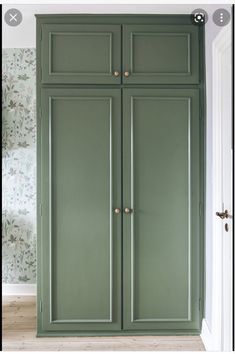 an empty room with green cupboards and wallpaper on the walls, in front of a white door