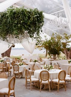 tables and chairs are set up under a canopy for an outdoor wedding reception with greenery hanging from the ceiling