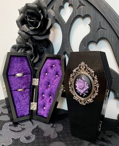 an open black box sitting on top of a table next to a purple rose and brooch