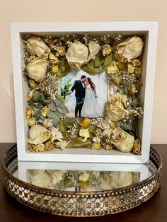 a wedding photo frame with flowers and leaves in the center on a table next to a platter