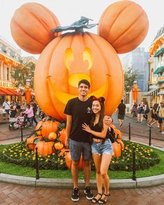 a man and woman standing in front of a mickey mouse pumpkin