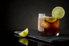 a close up of a drink on a table with lemons and lime wedges