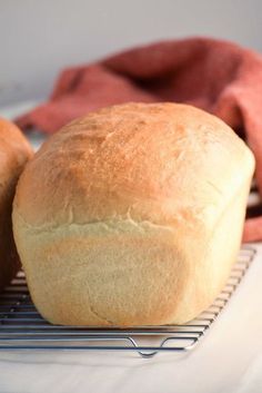 two loaves of bread sitting on a cooling rack next to a red towel and napkin