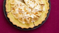 a pie with bananas and whipped cream on top sits on a purple tablecloth, ready to be eaten