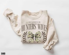 You will love this hunter's wife sweatshirt.  It says, "deserted hunters' wives social club".  This funny crewneck sweatshirt will be perfect for those wives of hunters to wear during hunting season.   Gildan 18000 Unisex Sweatshirt Details:  * Material: 50% cotton, 50% polyester  * Fabric Weight: Medium-heavy (8.0 oz/yd² or 271.25 g/m²)  * Fit: Loose fit for comfort  * Label: Sewn-in for a polished finish Care Instructions: * Machine wash warm (max 40oC or 105oF) * Non-chlorine bleach as needed Hunters Wife, Wife Sweatshirt, Funny Hunting, Coquette Top, Hunting Humor, Cute Coquette, Sweatshirt Details, Bow Sweater, Womens Camo