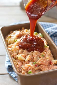 someone pouring ketchup on some food in a pan