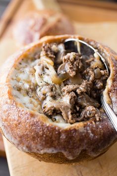 a close up of food in a bread bowl on a cutting board with a spoon