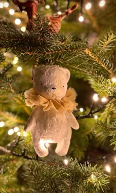 a teddy bear ornament hanging from a christmas tree with lights in the background