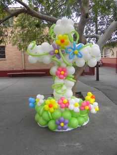 a balloon sculpture in the shape of a cross with flowers and butterflies on it, sitting next to a tree