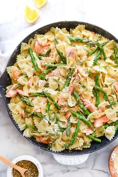 a skillet filled with pasta, asparagus and salmon on top of a marble counter