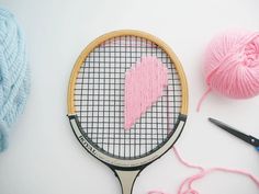 a tennis racquet and ball of yarn on a white surface with pink crochet