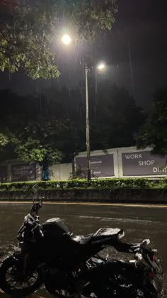 a motorcycle is parked on the side of the road in the rain at night time