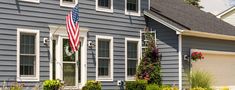 an american flag hanging on the side of a gray house with white trim and windows