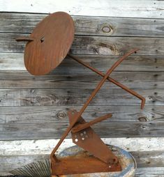 a rusty metal sculpture on top of a wooden table next to a wood plank wall