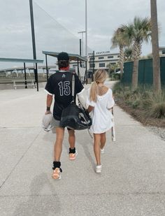 a man and woman walking down the street with baseball equipment on their back's