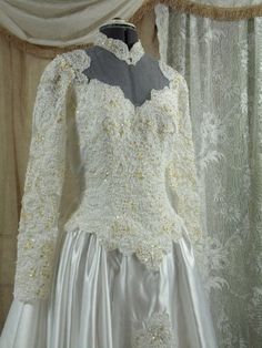 a white wedding dress with gold lace on the neckline and long sleeves is displayed in front of a curtain