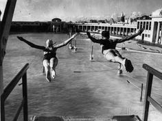 black and white photograph of two people jumping in the air with their hands out to each other