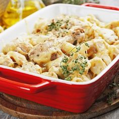 a red casserole dish filled with pasta and meat, garnished with parsley