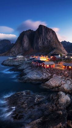 an island with houses on the shore and mountains in the background at night, lit up by street lights