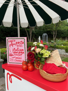 there is a sign and some flowers on the red table with it's umbrella