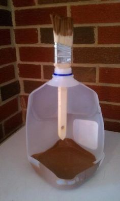 a plastic bottle with a brush sticking out of it sitting on a table next to a brick wall