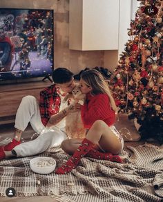 a man and woman sitting on the floor in front of a christmas tree with their dog