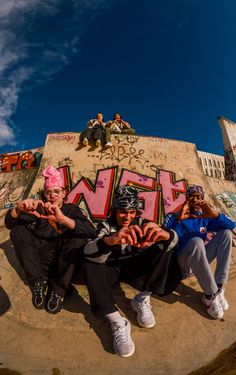 three people sitting on top of a skateboard ramp with graffiti painted on the walls