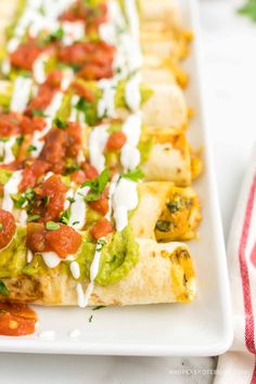 a white plate topped with tacos covered in guacamole and salsa sauce