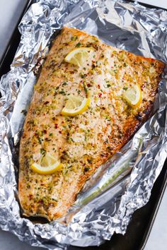 a piece of fish with lemons and herbs on it sitting on tin foil in a pan