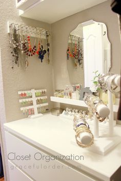 a white dresser topped with lots of jewelry next to a wall mounted mirror and two mirrors