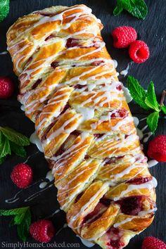 croissant with raspberries and cream drizzled over it on a black surface