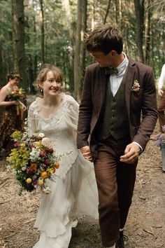 a bride and groom walking through the woods