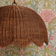 a wicker light fixture hanging from a wall with floral wallpaper in the background