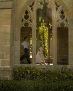 a man and woman are walking in front of an arched window with ivy growing around it