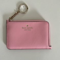 a pink purse with a key chain hanging from it's front pocket on a white surface