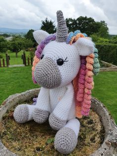 a crocheted stuffed unicorn sitting on top of a plant pot in the grass