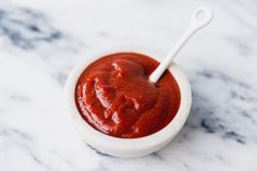 a small white bowl filled with sauce on top of a marble countertop next to a spoon