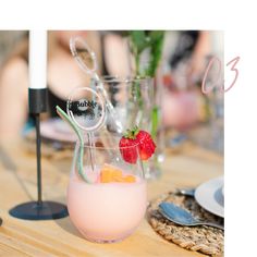 a glass filled with pink liquid sitting on top of a wooden table