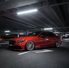 a red car is parked in a parking garage with its lights on and it's hood up