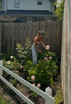 a woman is tending to some flowers in the garden outside her house on a sunny day