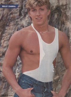 a shirtless young man standing in front of a rock wall with his hands on his hips